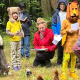 Children in brightly coloured cothes and hand-made animal costumes, reciting a play in the forest with their teacher, looked on by their parents