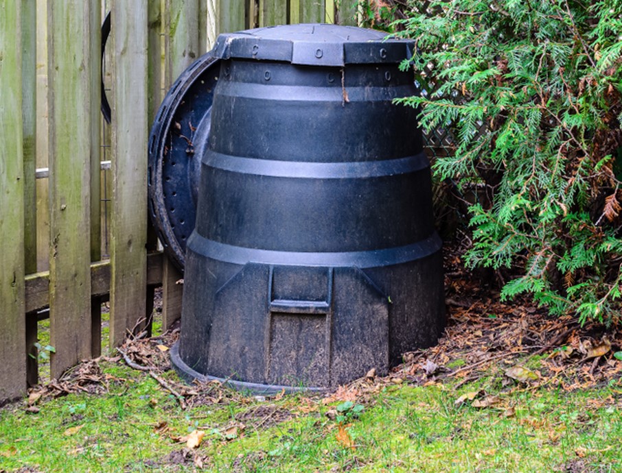 Backyard composter next to a fence and hedge